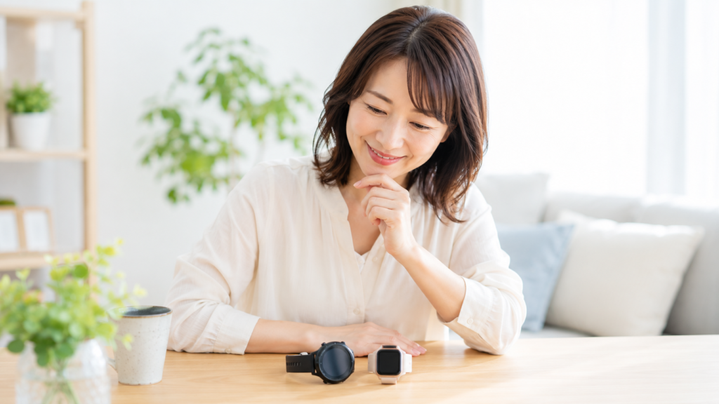 丸型と角型の2本のスマートウォッチを見比べる女性のイメージ。ガーミンとアップルウォッチで迷う場面