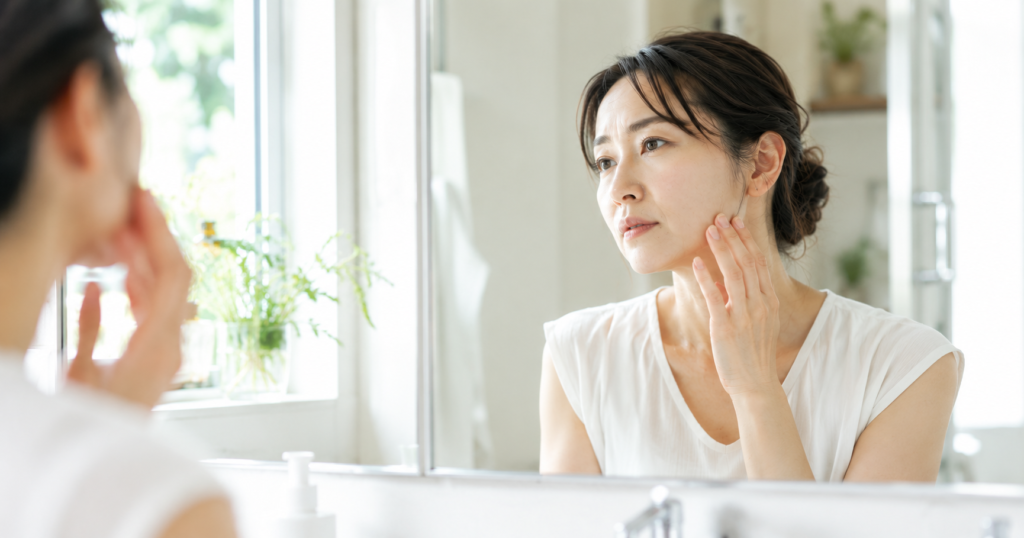 鏡の前でフェイスラインのたるみを確認している40代女性。顔のたるみと巻き肩の関係を解説する記事のイメージ